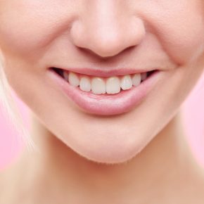 Close-up of lower part of face of young healthy female with toothy smile and natural makeup in isolation